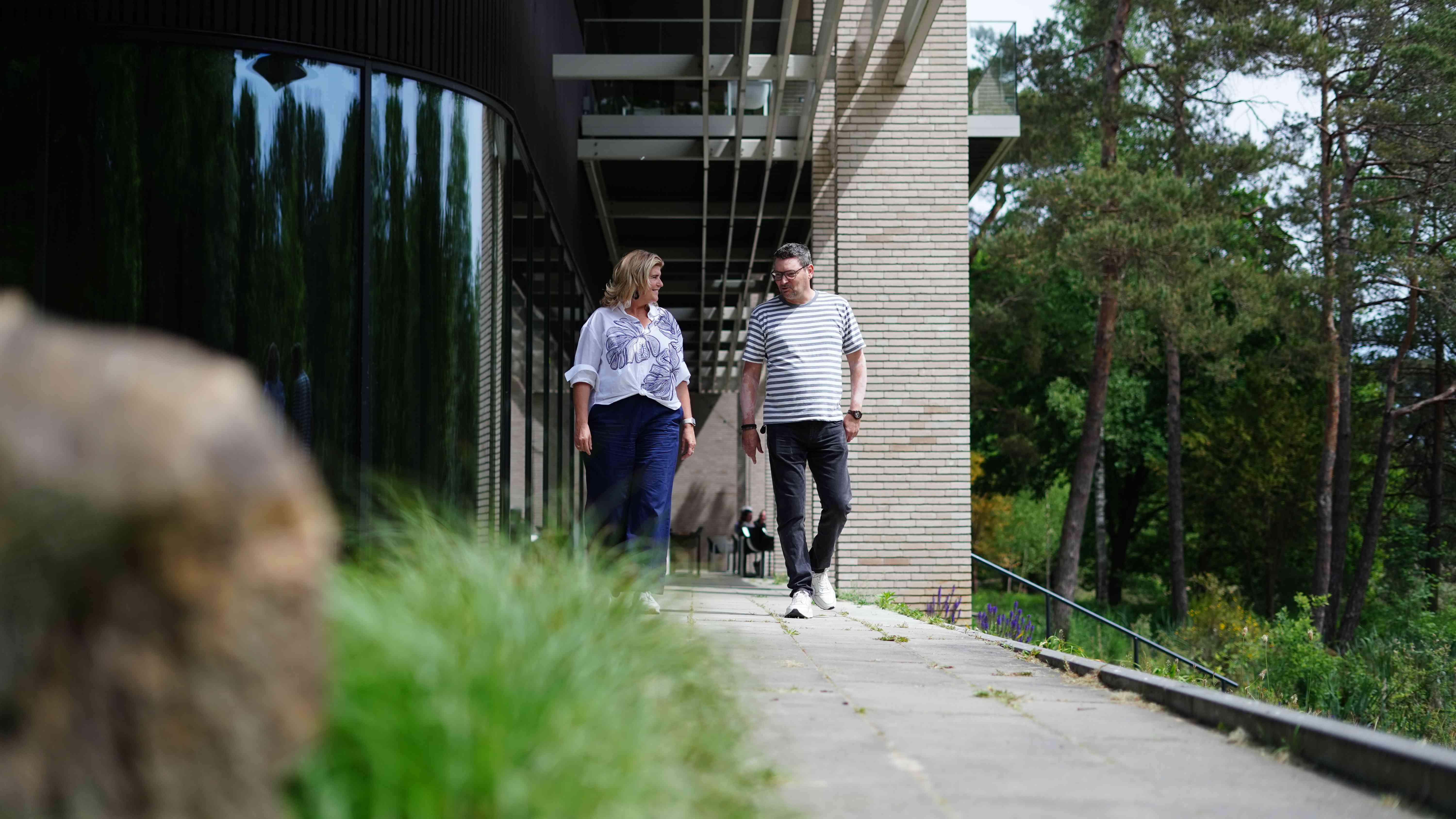 Twee medewerkers lopen achter het gemeentehuis en lachen naar elkaar